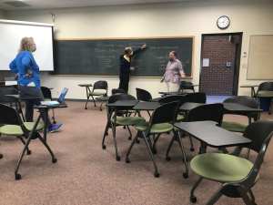 Man reaching to write on the chalkboard, woman standing nearby