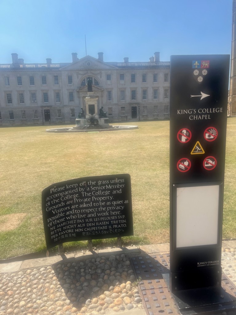 A sign in the foreground reads, "Please keep off the grass unless accompanied by a Senior Member of the College. The College and Grounds are Private Property. Visitors are asked to be as quiet as possible and to respect the privacy of those who live and work here." The directive to "keep off the grass" is translated into French, German, Italian, Chinese, and Japanese.